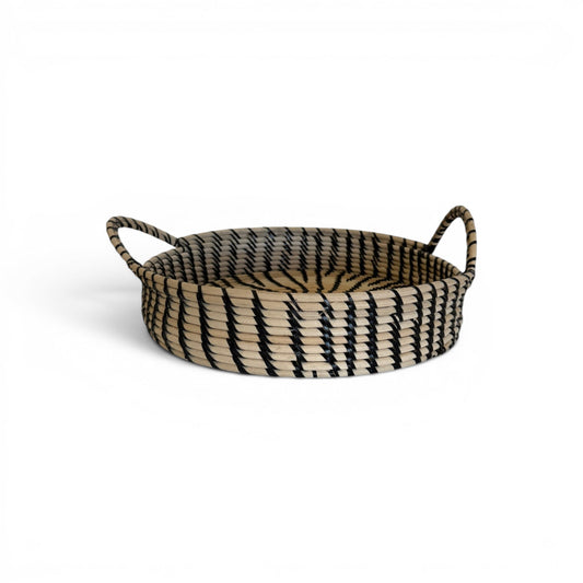 Large circular hand-woven rattan decorative tray with a black and cream graphic tribal pattern and two integrated loop handles.