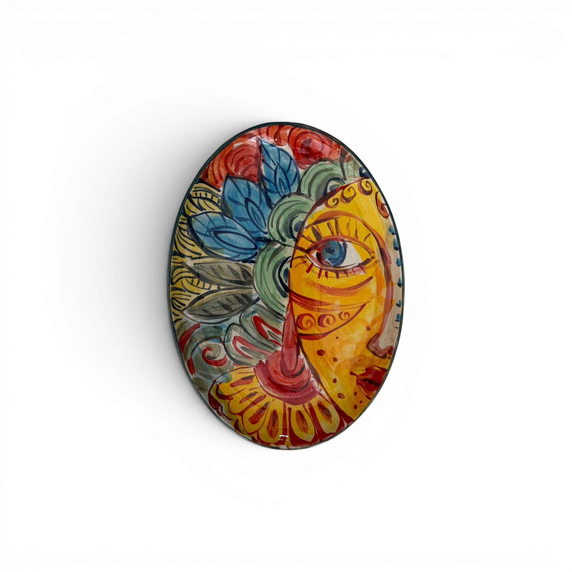 An oval decorative plate featuring a vibrant, hand-painted style illustration of a face with blue flowers and green leaves, shown against a plain white background.